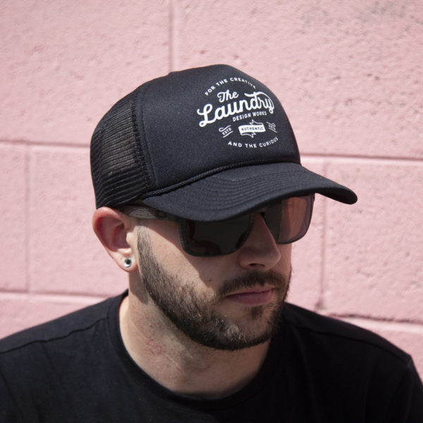 Man wearing sunglasses and a black retro foam trucker hat featuring a retro style Laundry Design Works logo graphic